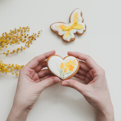  gingerbread cookie in a shape of a heart and mimosa flowers on white background. top view copy space