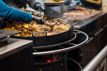 the seller fries meat and potatoes in a large cauldron at the fair. street fast food