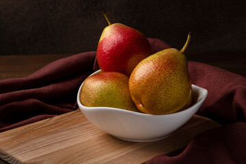 Trout pears. Several fruits are in a white bowl. Close-up, brown background, horizontal orientation.