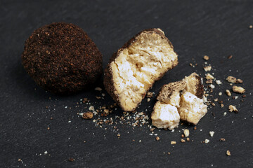 A whole and broken ball of Belper Knoll cheese lies on a black slate board. Hard Swiss cheese. side view.