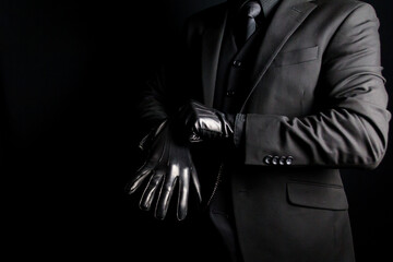 Portrait of Man in Dark Suit Pulling on Leather Gloves on Black Background. Gentleman Killer or...