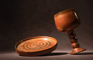 A decorative plate in antique style and a drinking cup stand on a dark dusty pink background. The concept of handmade ceramic tableware. Selective focus, balancing dishes.