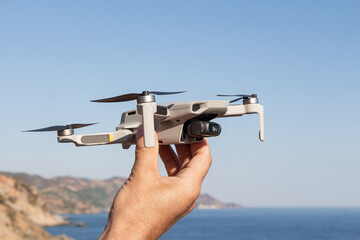 Man is launching a gray drone with a with four propellers and blades in his hands in sunny summer day