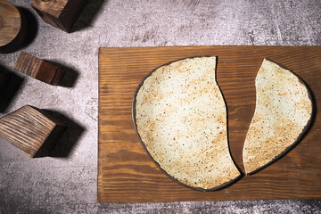 A handmade ceramic plate, broken in half, lies on a wooden board on a gray background with wooden objects of different shapes. Deconstruction concept, top view, close-up