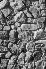 stones and oddly shaped rocks puzzle pieced together to create stone or rock masonry retaining wall in black and white  vertical format room for type background wallpaper or backdrop shades of grey 