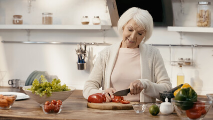 Obraz na płótnie Canvas smiling senior woman cutting bell pepper while preparing thanksgiving dinner.