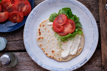Flatbread with sauce, tomato, lettuce. Wooden background, top view