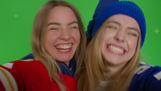 Two girls making selfie. Funny hipster females making self portrait . Young women in casual clothes having fun in front of green screen background. Chroma key