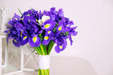 Bouquet of irises flower with white roses and white decorative lantern on beige background. Closeup, front view, copy space.