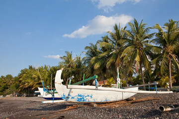 Obraz na płótnie Canvas Colorful outrigger fishing boats on a shady beach in Bali Indonesia with sunny blue sky overhead