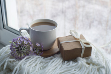 a cup of cocoa, gift box, a primrose flower on a white knitted scarf. congratulations on March 8, gift to mom, romantic background. 