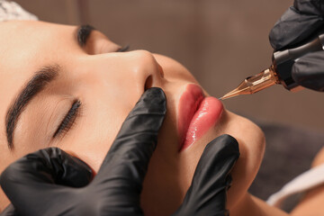 Young woman undergoing procedure of permanent lip makeup in tattoo salon, closeup - obrazy, fototapety, plakaty
