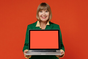 Elderly woman 40s in green classic suit hold use work on laptop pc computer with blank screen workspace area isolated on plain orange color background studio portrait People business lifestyle concept