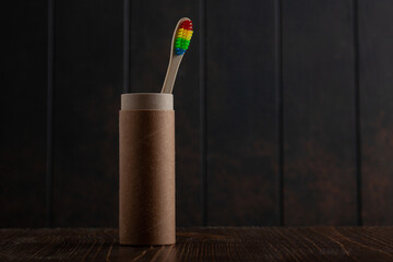 Rainbow colored bamboo toothbrush in a paper cup on a dark wooden background. Zero waste. Copy...