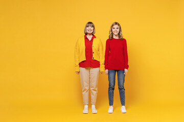 Full body smiling happy cool woman 50s in red shirt have fun with teenager girl 12-13 years old. Grandmother granddaughter look camera isolated on plain yellow background. Family lifestyle concept