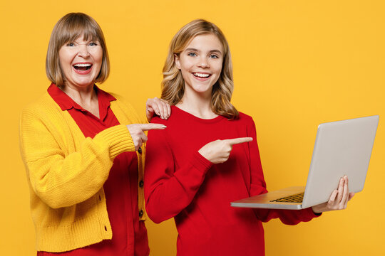 Smiling Cool Woman 50s In Red Shirt With Teenager Girl 12-13 Years Old Grandmother Granddaughter Hold Use Work Point On Laptop Pc Computer Isolated On Plain Yellow Background Family Lifestyle Concept