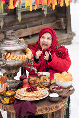Shrovetide concept Maslenitsa. Joyful little girl licks a traditional russian Lollipop in shape of rooster, sits at a table with a samovar and pancakes.