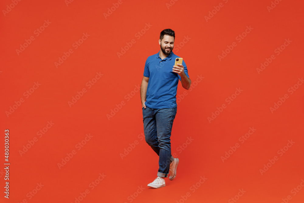 Canvas Prints Full body young smiling happy caucasian man wear basic blue t-shirt hold in hand use mobile cell phone browsing internet isolated on plain orange background studio portrait. People lifestyle concept.