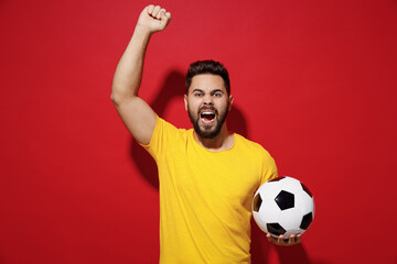 Exultant fun young bearded man football fan in yellow t-shirt cheer up support favorite team hold...
