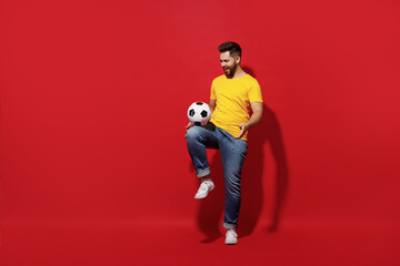 Full size body length young bearded man football fan in yellow t-shirt cheer up support favorite team juggling soccer ball isolated on plain dark red background studio portrait. Sport leisure concept.