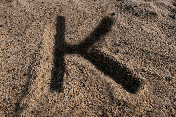 English alphabet. Sand on the beach. The letter K