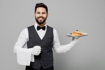 Young happy barista male waiter butler man wear white shirt vest elegant uniform work at cafe hold cheesecake waffles isolated on plain grey background studio portrait. Restaurant employee concept. - obrazy, fototapety, plakaty