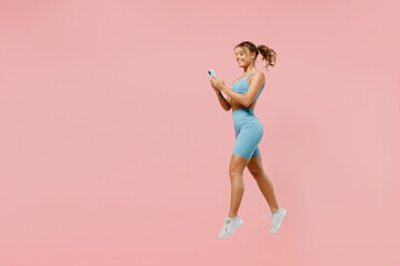 Fototapeta na wymiar Full body young sporty athletic fitness trainer woman wear blue tracksuit spend time in home gym jump high use mobile cell phone isolated on pastel plain light pink background. Workout sport concept.