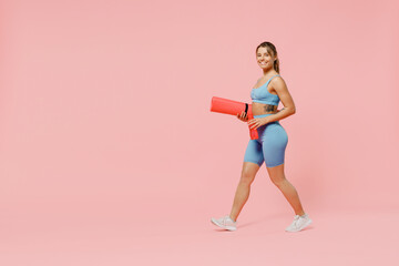 Fototapeta na wymiar Full size young strong sporty athletic fitness trainer instructor woman wear blue tracksuit spend time in home gym hold caremat walk go isolated on plain light pink background Workout sport concept.