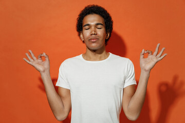 Naklejka premium Spiritual tranquil young black curly man 20s wears white t-shirt hold spreading hands in yoga om aum gesture relax meditate try to calm down isolated on plain pastel orange background studio portrait.
