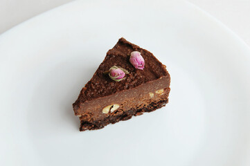 Slice of vegan chocolate nut cake on white plate close-up top view