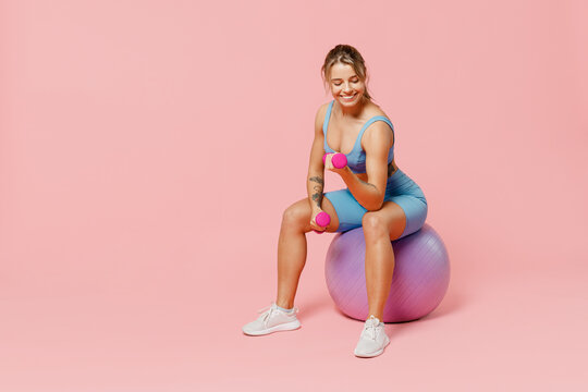 Full length young strong sporty athletic fitness trainer instructor woman wear blue tracksuit spend time in home gym sit fitball isolated on pastel plain light pink background Workout sport concept