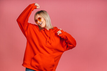 Photo of cheerful beautiful young woman standing isolated on pink wall background. Watching the camera showing the gesture of the winner.