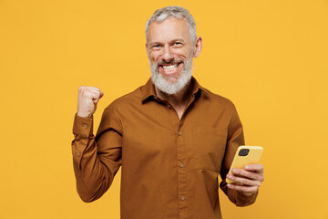 Jubilant happy elderly gray-haired bearded man 40s years old wear brown shirt look camera hold use...