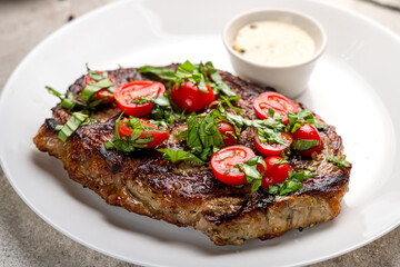 juicy Ribeye steak with fresh tomatoes on white plate on grey concrete table macro close up