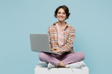 Full body young smiling cheerful happy cool woman 20s wear brown shirt sit on white chair hold use...