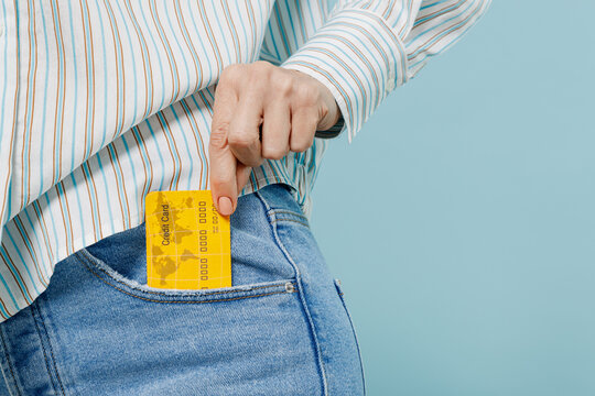 Close up cropped photo shot of caucasian woman wear striped shirt hold in hand credit bank card put into pocket isolated on plain pastel light blue background studio portrait People lifestyle concept