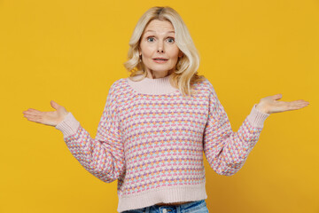 Elderly puzzled confused blonde caucasian woman 50s in pink sweater shrugging shoulders looking...