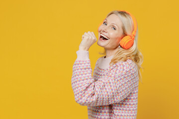 Elderly smiling fun blonde caucasian woman 50s in pink sweater headphones listen to music sing song...