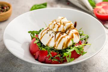 Salad with buratta cheese and tomatoes on plate on grey concrete table macro close up