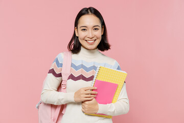 Teen student smiling happy fun girl of Asian ethnicity 20s wearing sweater backpack hold books isolated on pastel plain light pink color background Education in high school university college concept.