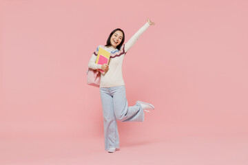 Full body smiling happy cheerful teen student girl of Asian ethnicity in sweater hold backpack book stretch hand isolated on pastel plain light pink background Education in university college concept.