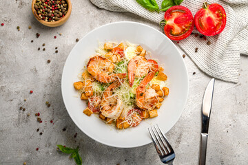 salad caesar with shrimps on white plate on grey concrete table top view