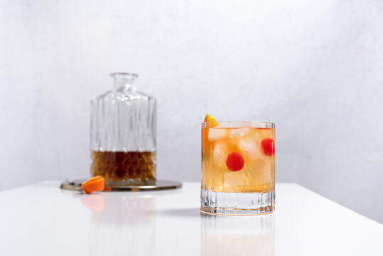 Vaso de vermut con hielo decorado con una rodaja de naranja y cereza sobre mesa blanca	