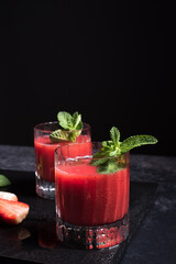 Dos vasos de refrescante jugo de fresa triturado decorado con una rama de menta y fresas cortadas sobre un fondo negro	
