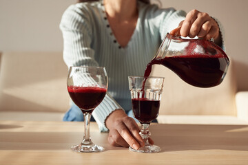 Female hands pouring beetroot juice from a jug into glasses