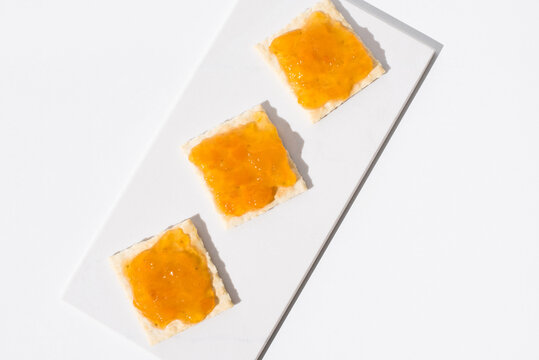 Mermelada de albaricoque sobre pan tostado en una mesa blanca y fondo claro. Vista superior