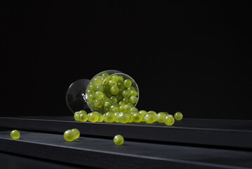 Uvas de vino blanco verdejo español en una copa de vino caída sobre una mesa de madera negra y fondo negro