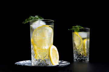 Dos vasos de refrescante zumo de limón, cóctel de frutas con rodajas de limón y hielo sobre fondo negro