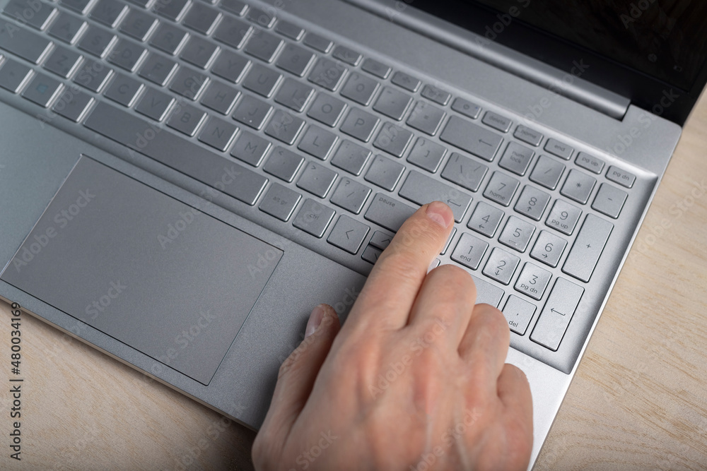 Poster hand on laptop keyboard, tapping and pressing button with finger closeup.