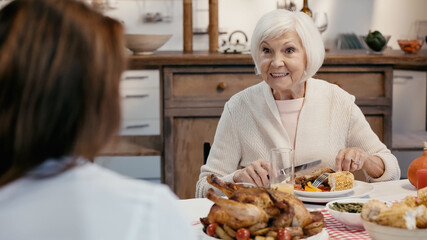senior woman smiling during thanksgiving dinner with blurred guest.